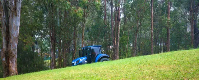 A blue tractor working across a green hill.