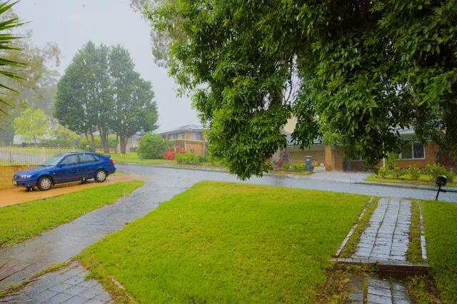 A blue car parked and the view of a footpath out of a house. Taken from the porch.