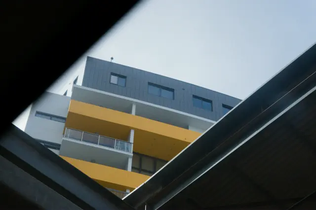 A shot of a building with yellow balconies. Shot from underneath and framed by the train station roofing.
