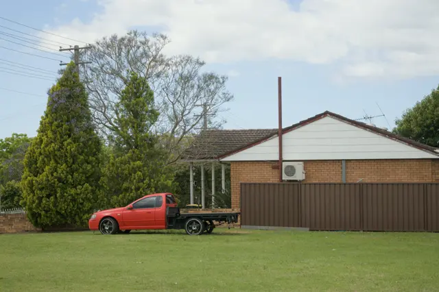 Red truck in front of trees and a house