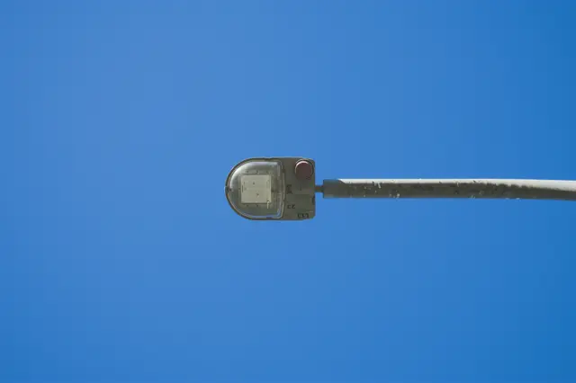 Photo of a street lamp from underneath, against a perfectly blue sky. The lamp has some markings that give it anime-mech vibes.