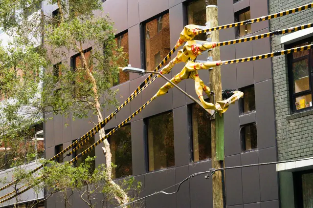 Yellow and black warning/protective tape around power wires in a wooden pole. Building windows in the background.