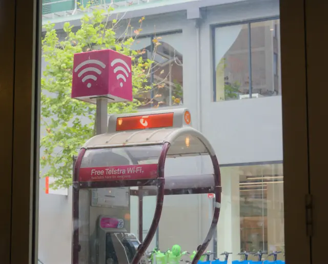 Telstra payphone. &ldquo;Free telstra Wi-Fi&rdquo; it says. A green tree in the background.