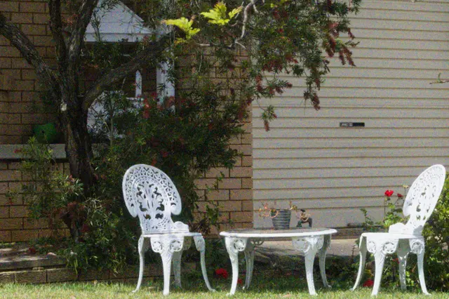 White lawn chairs and table in the shadow of a tree.