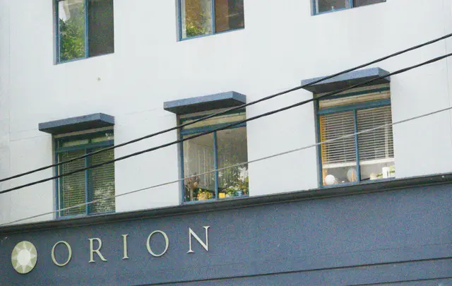 Building facade. &ldquo;ORION&rdquo; it says. In the center a window decorated with flowers.